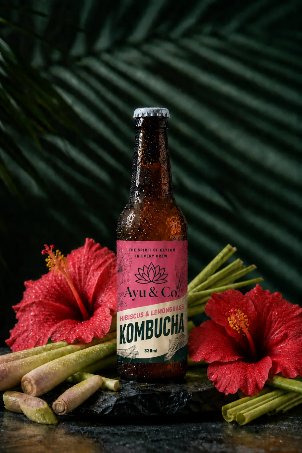 Ayu & Co. Hibiscus & Lemongrass Kombucha bottle surrounded by deep red hibiscus flowers and lemongrass stalks
